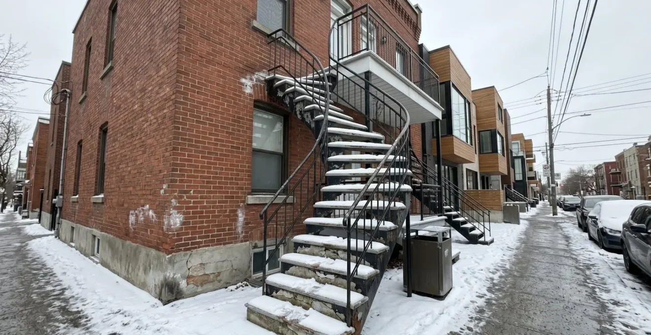 Escalier extérieur résidentiel avec marches en béton présentant des fissures visibles et un début d'effritement, accumulation de neige sur les côtés, architecture typique d'une maison montréalaise